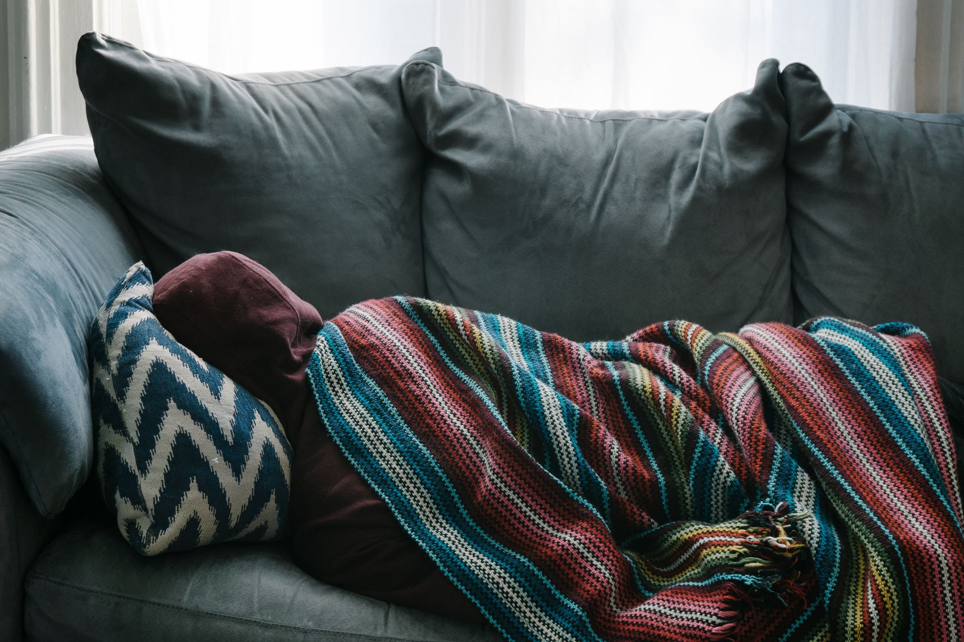 A person lying on the sofa covered in a blanket.