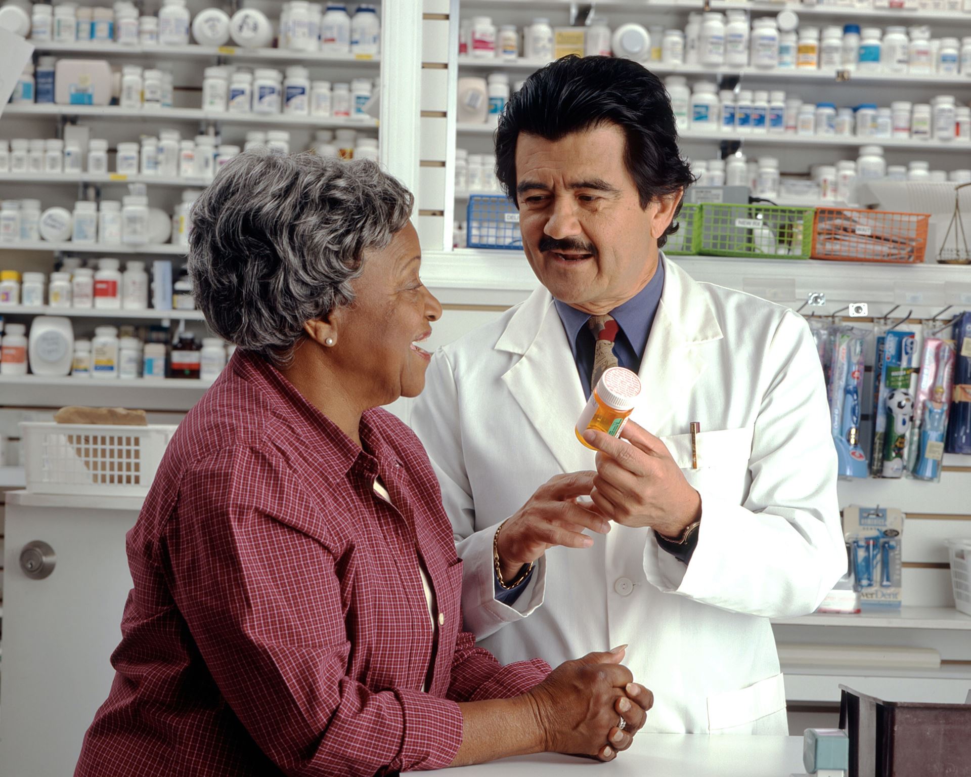 A pharmacist giving a bottle of pills to a lady with grey hair