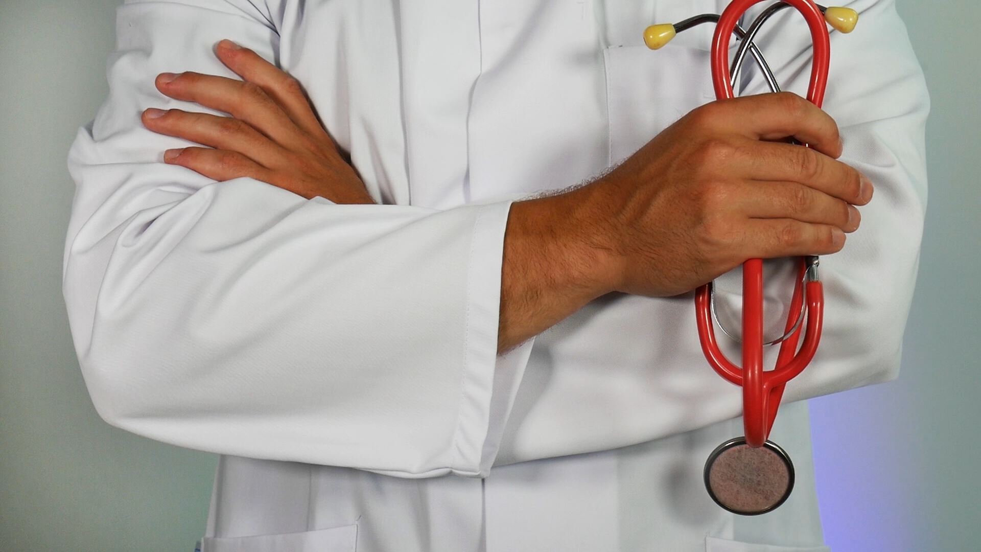 A person wearing a white coat holding a red stethoscope