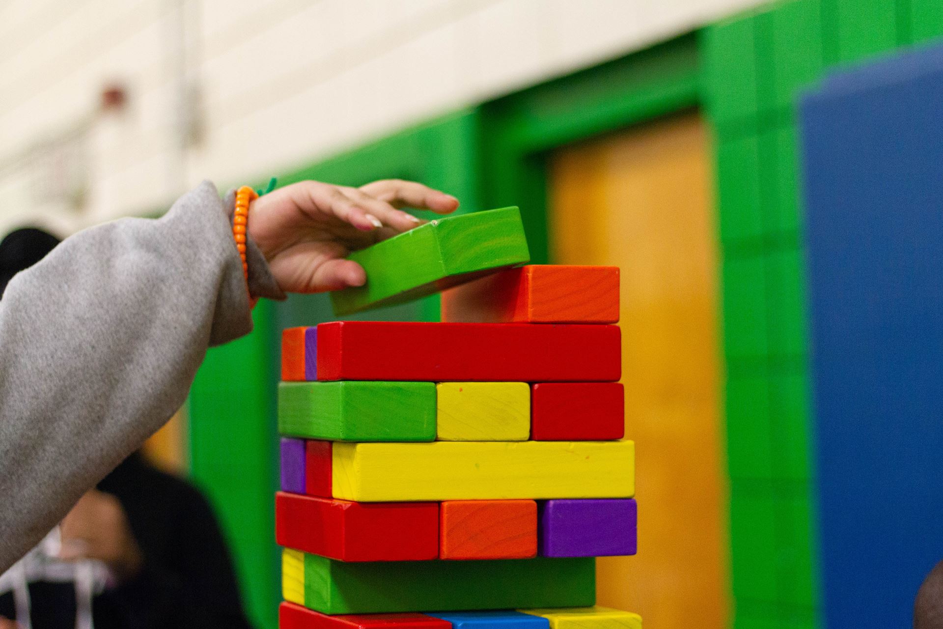 A child's hand lifting a jenga block onto the top of a tower