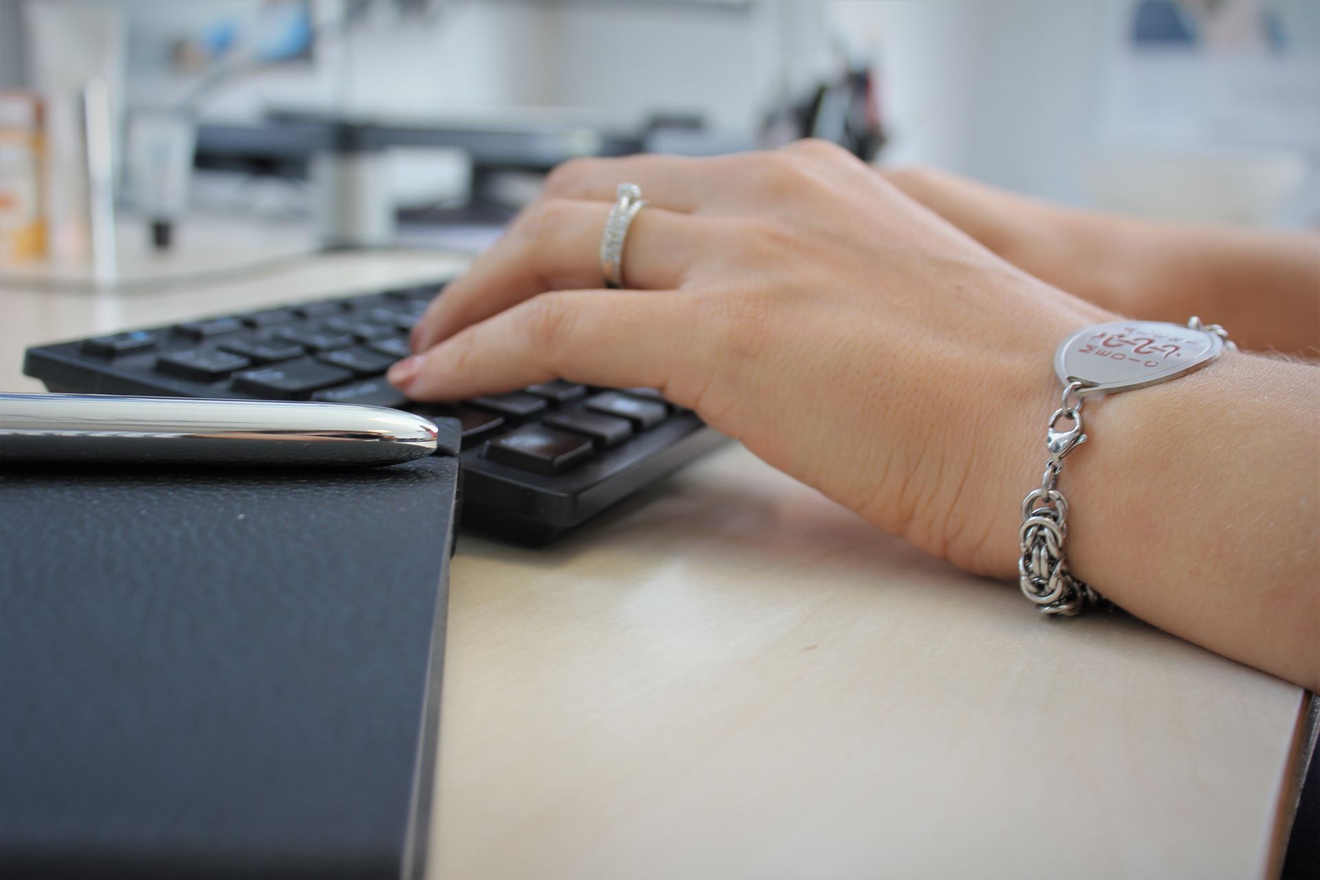 Hands typing on a keyboard. The hand nearest to us is wearing a bracelet and a ring.