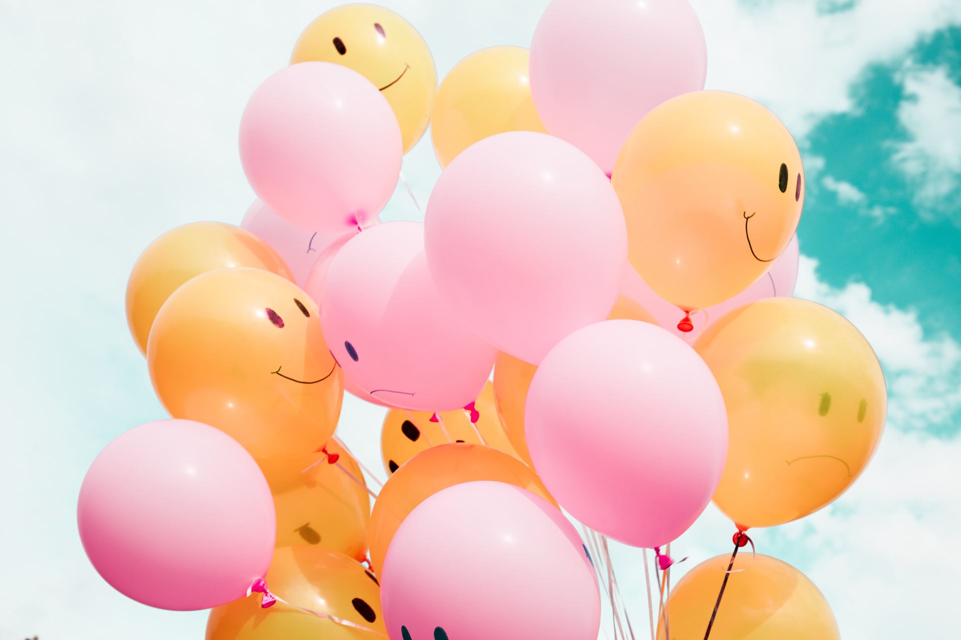 Pink and orange balloons, some of which have smiley faces